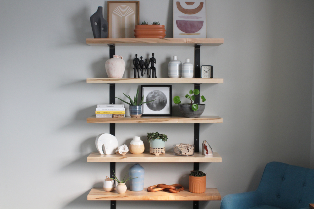 Wormy Maple Floating Bookshelf decorated with plants, statues, pictures and vases.