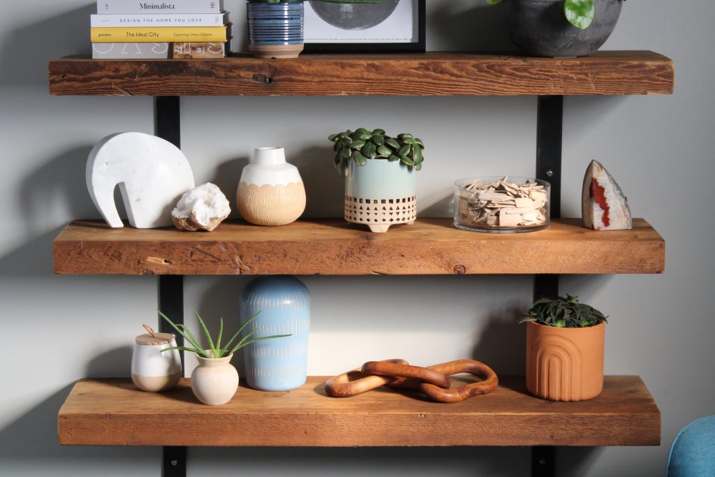 A Reclaimed wood floating bookshelf decorated with vases, succulents and other interior decor.